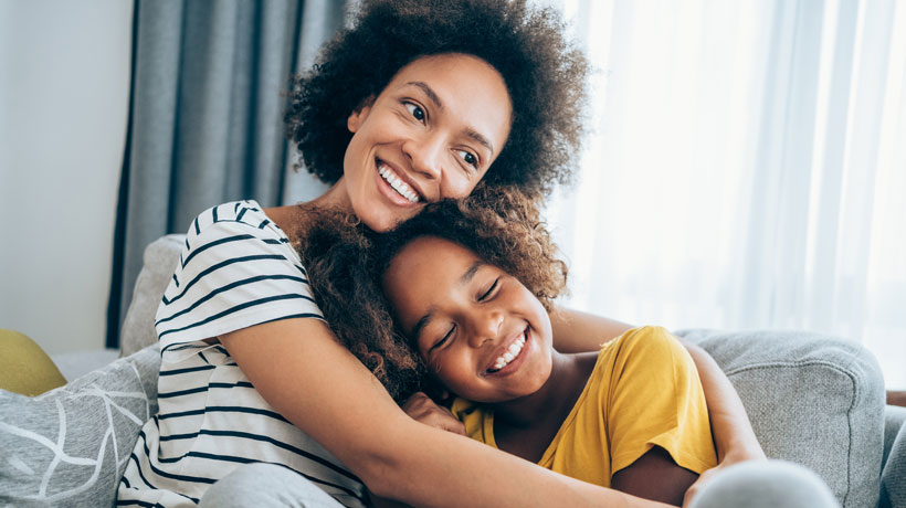 Une mère et sa fille souriantes qui se câlinent sur un canapé