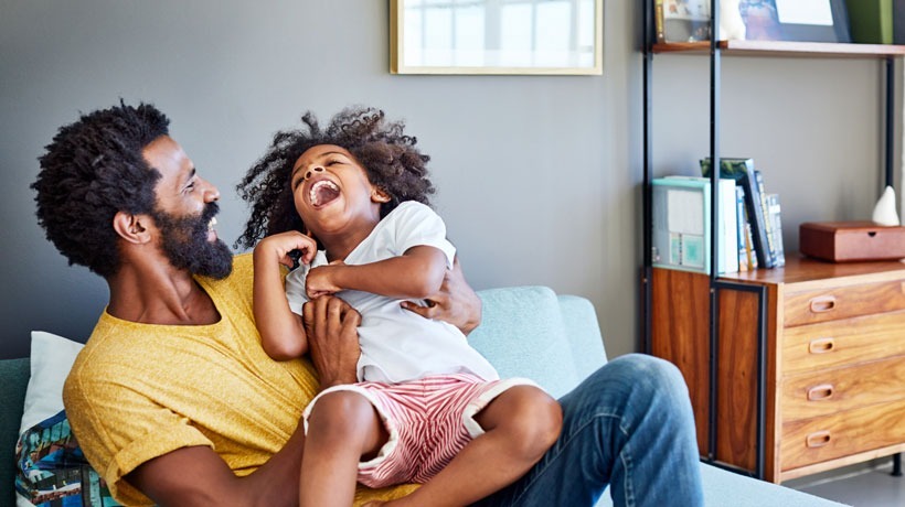 Un père avec sa fille qui joue et rient sur un canapé