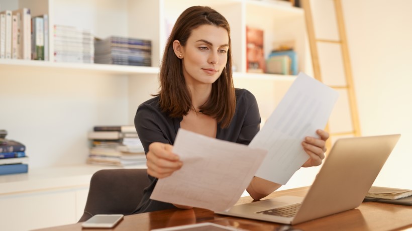 Femme qui travaille avec un ordi en regardant ses feuilles